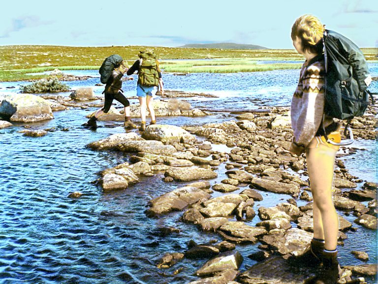 Hikers fording a river with backpacks, illustrating why a dry bag matters on multi-day trails